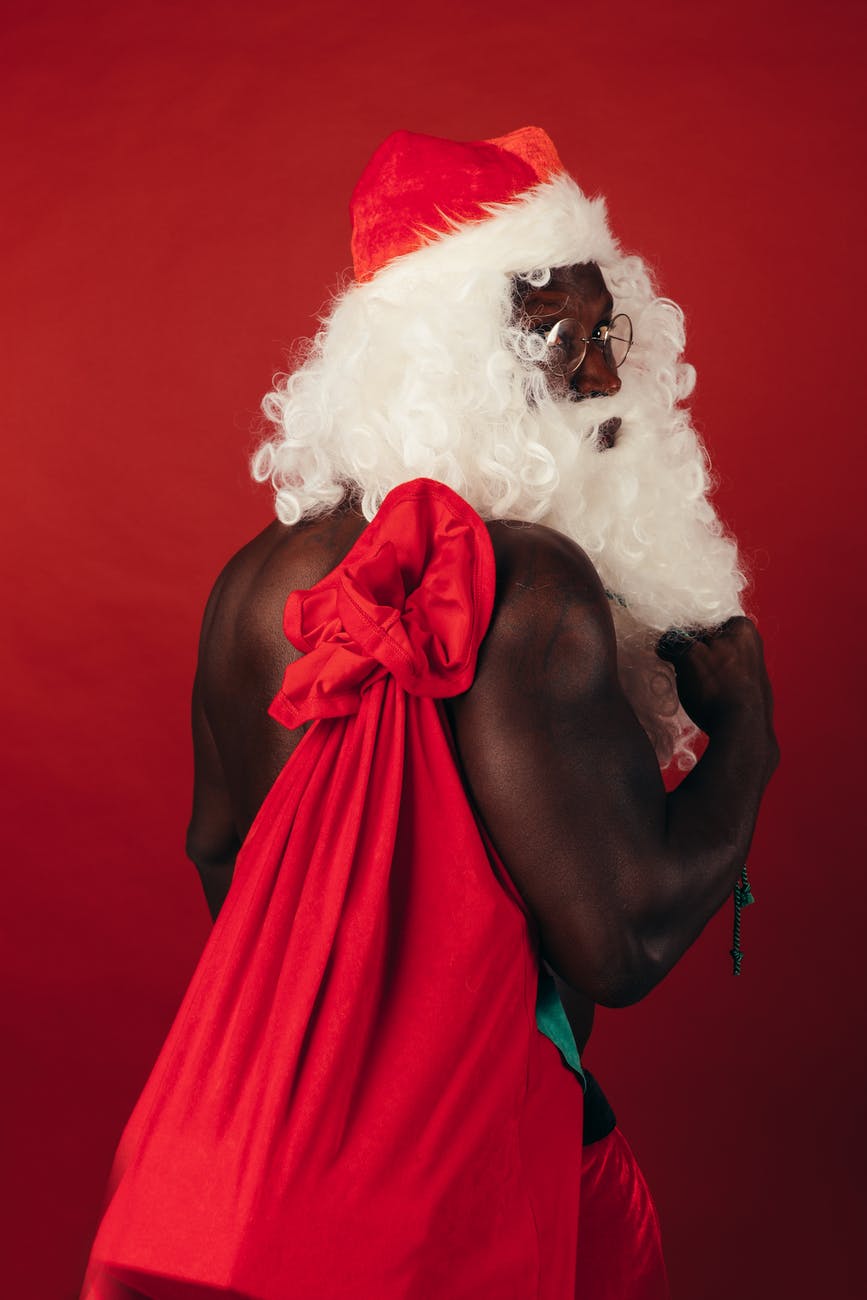 shirtless man in a santa outfit carrying gifts